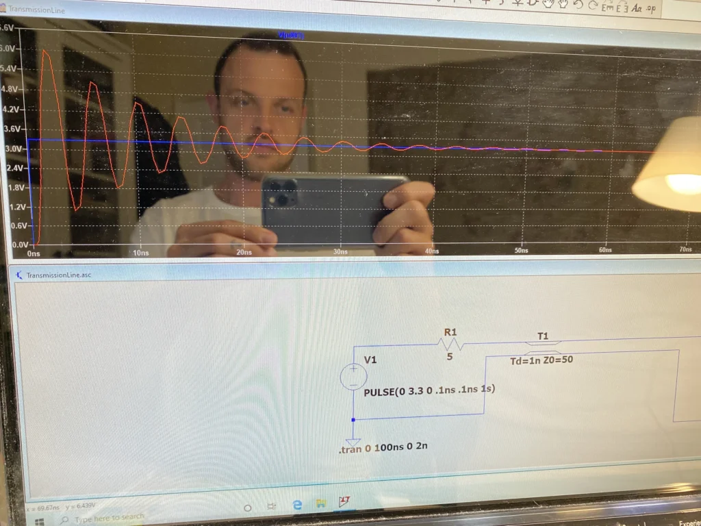 Man taking smartphone selfie reflected in computer screen displaying transmission line simulation with voltage waveforms and circuit schematic.