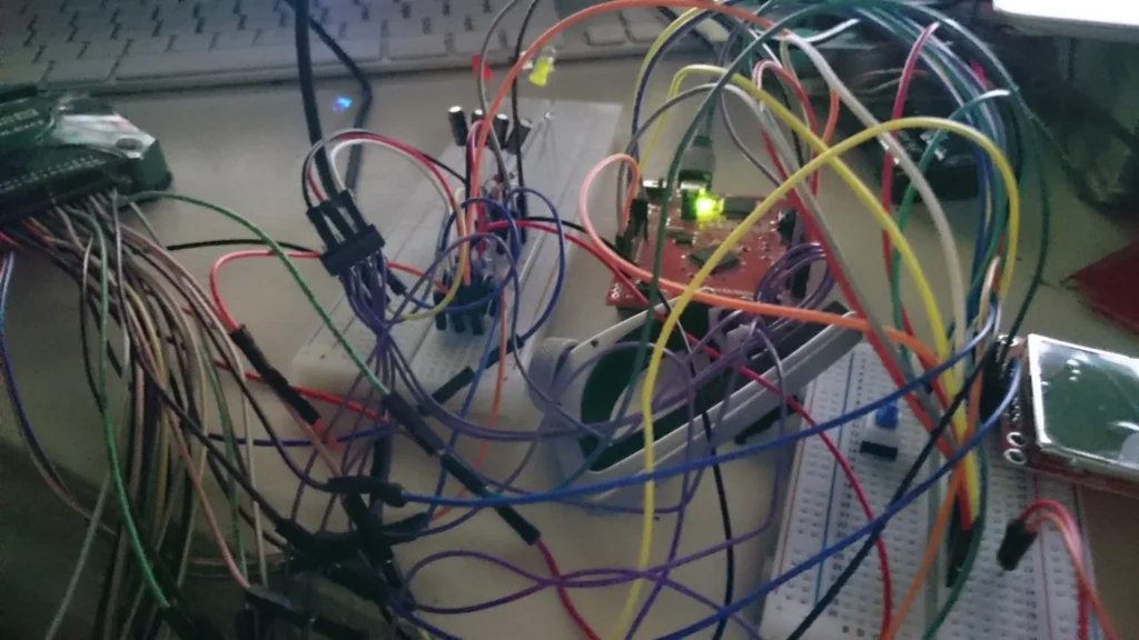Tangled multicolored wires connecting Arduino, breadboards, and electronic components on a desk near a keyboard.