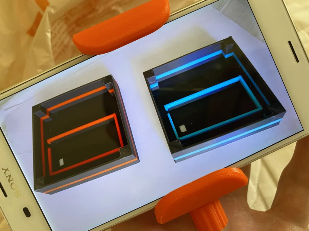 Orange phone mount holding smartphone displaying red and blue glowing square frames on white surface.