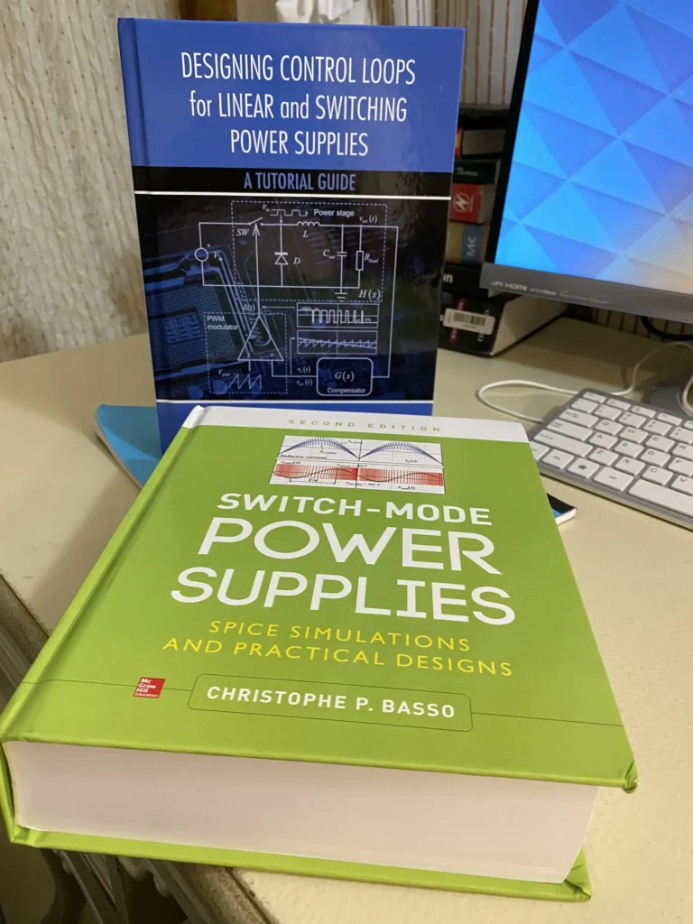 Two open books on power supply design and SPICE simulations on a desk beside a computer monitor and keyboard.