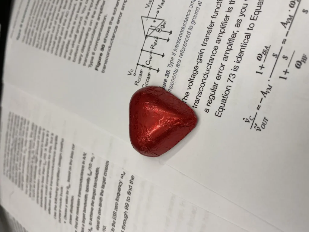 Heart-shaped foil-wrapped chocolate on open electronics textbook pages with amplifier schematics and equations.