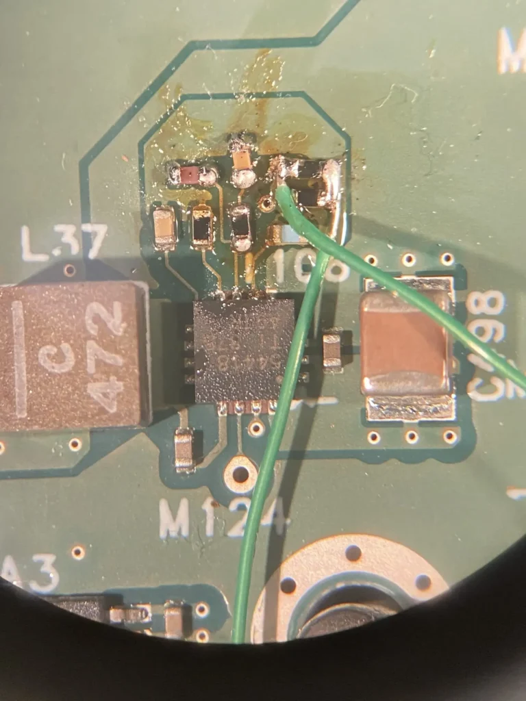 Close-up of green PCB with black IC chip, green wire, capacitors labeled L37, C472, and solder joints under magnification.