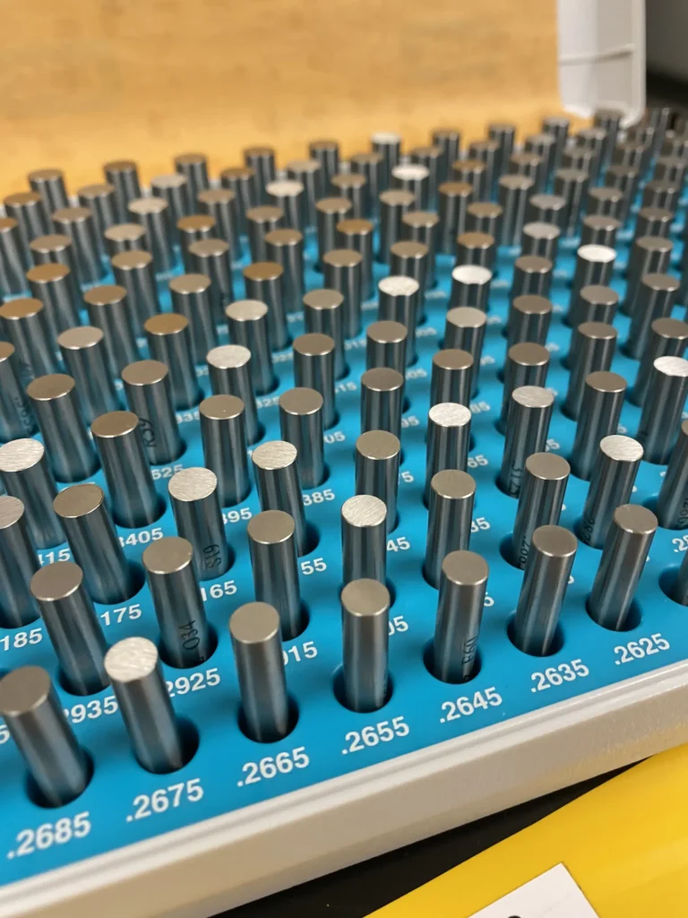 Close-up of precision pin gauges of varying sizes labeled with measurements in a blue tray.