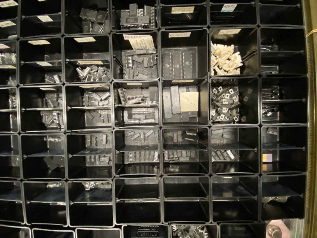 Black plastic organizer bins filled with assorted integrated circuits, chips, and electronic components.