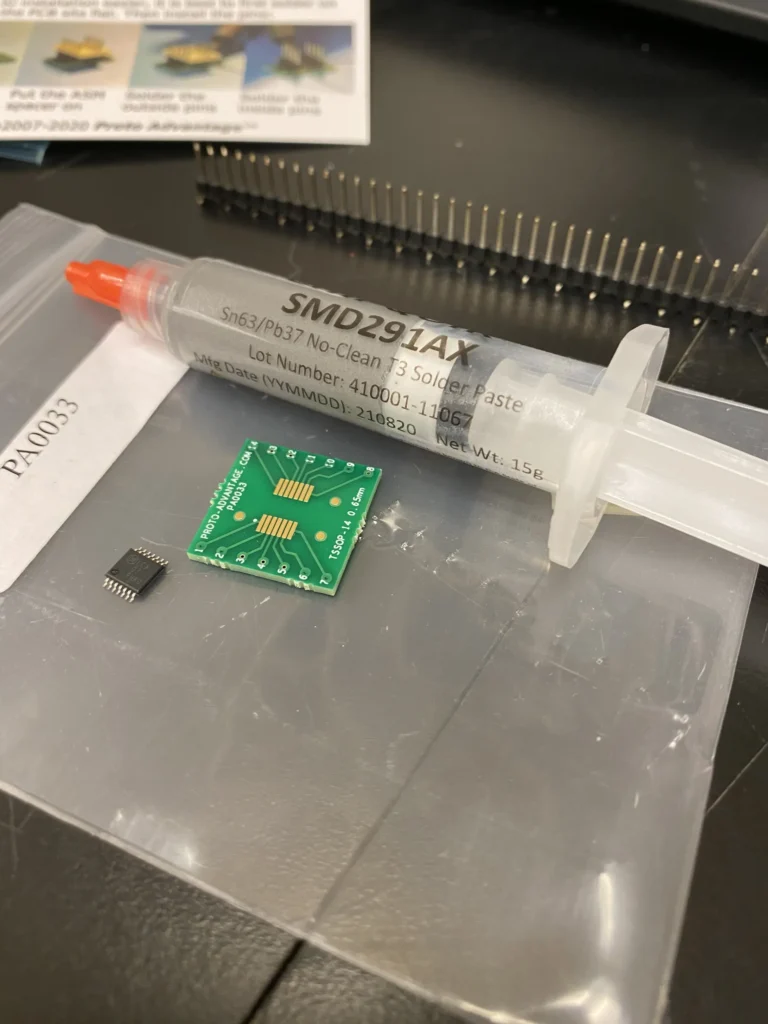 SMD291AX no-clean solder paste syringe, prototype PCB, and SMD chip on a workbench.