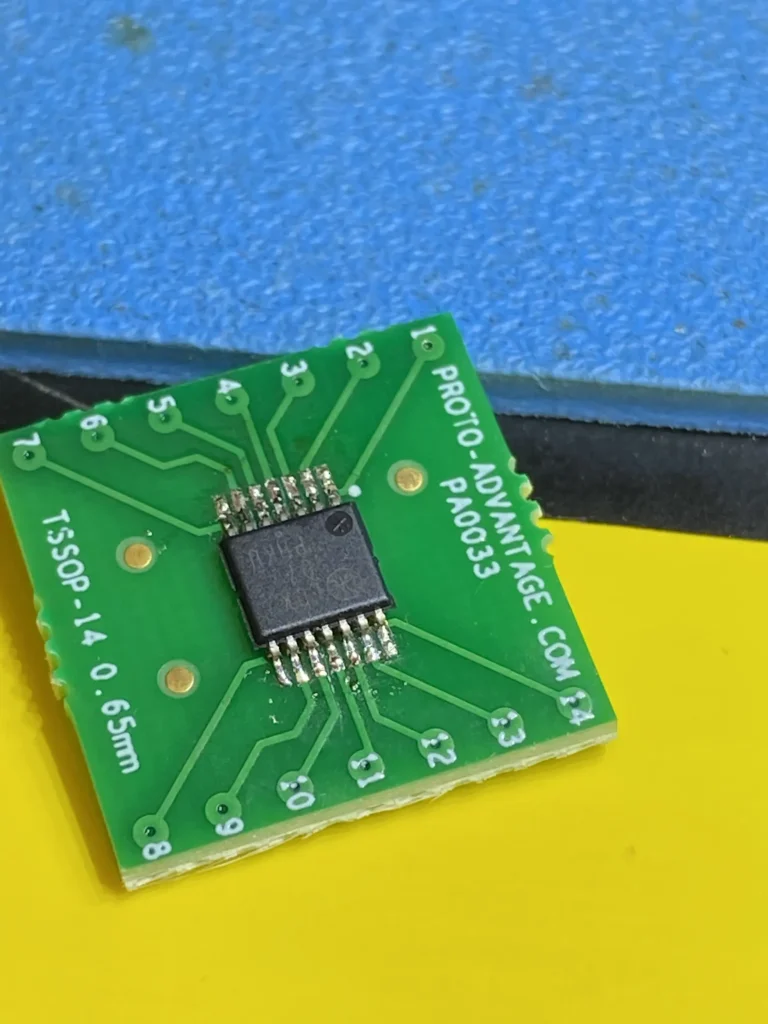 Green TSSOP-14 protoboard adapter PCB with central IC on yellow and blue surface.