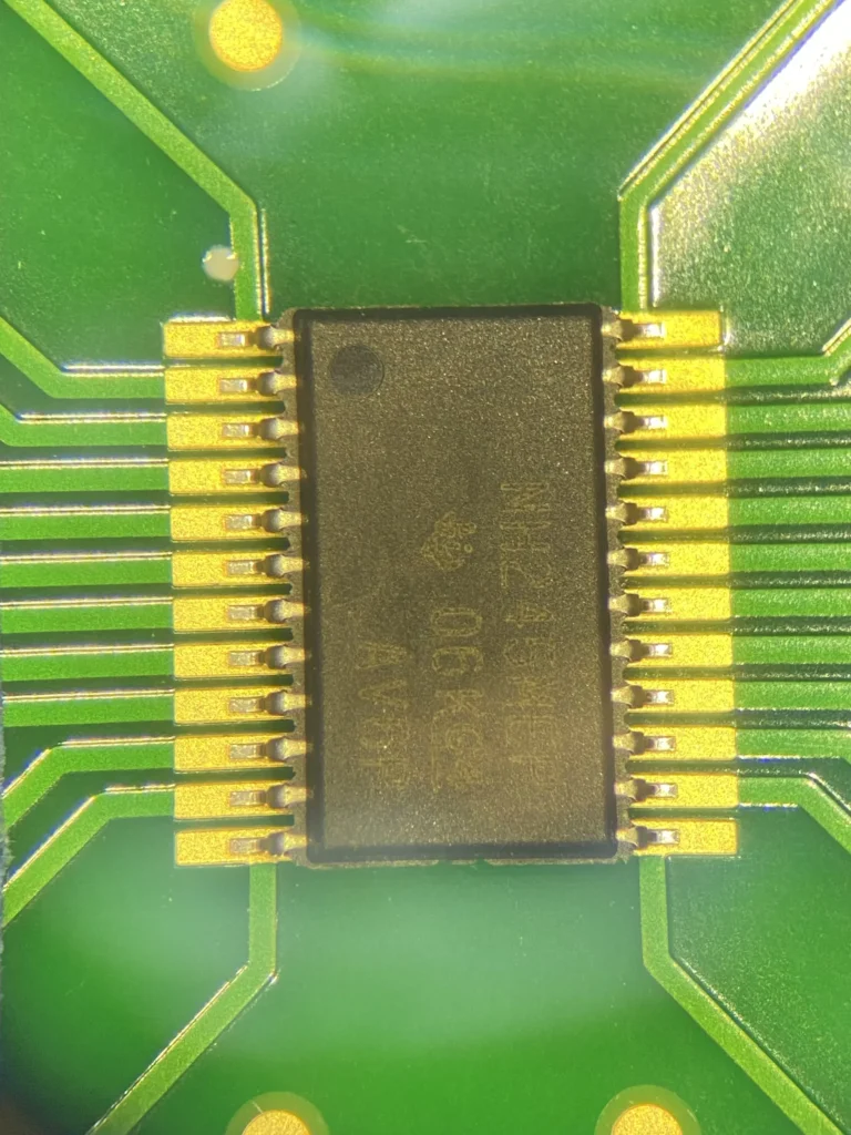 Close-up of a black 20-pin IC chip soldered onto a green PCB with gold leads and traces.