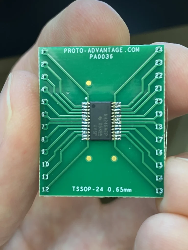 Close-up of green TSSOP-24 adapter PCB (Proto-Advantage PA0036) held in fingers with central NH RS485 chip.