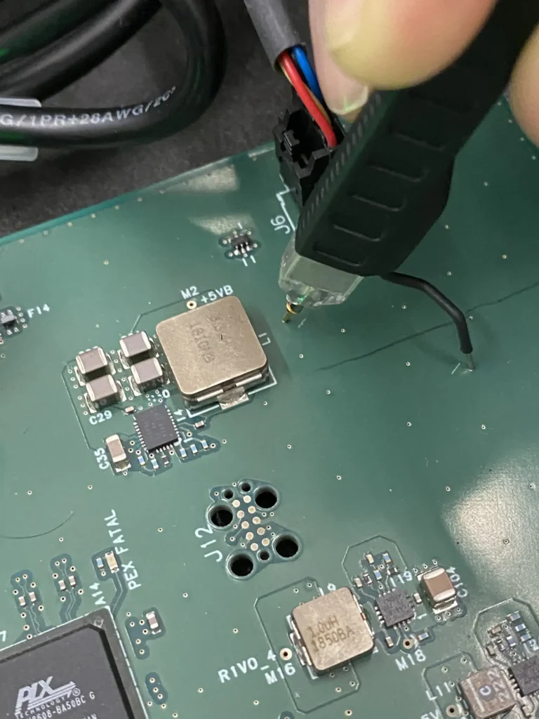 Hand soldering thin red and blue wires onto a green Vivo motherboard with a black soldering iron.