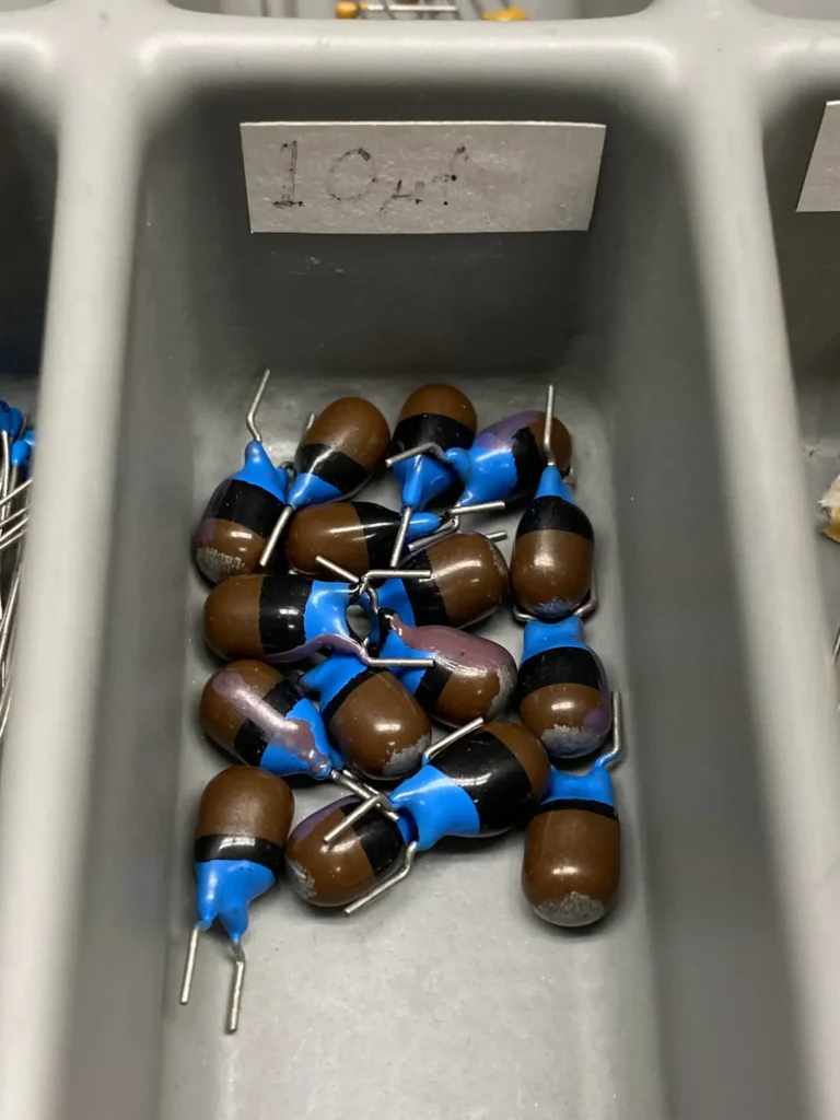 104 brown electrolytic capacitors with blue insulators in a gray bin tray.