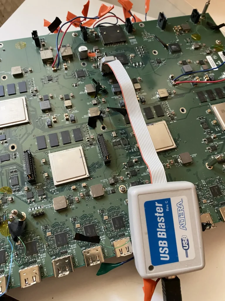 Green motherboard with chips, connectors, ribbon cable, and attached USB Blaster debugger.