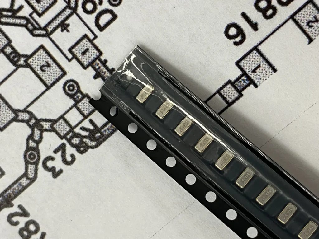 Strip of JPL464A SMD components on tape over a PCB schematic diagram.