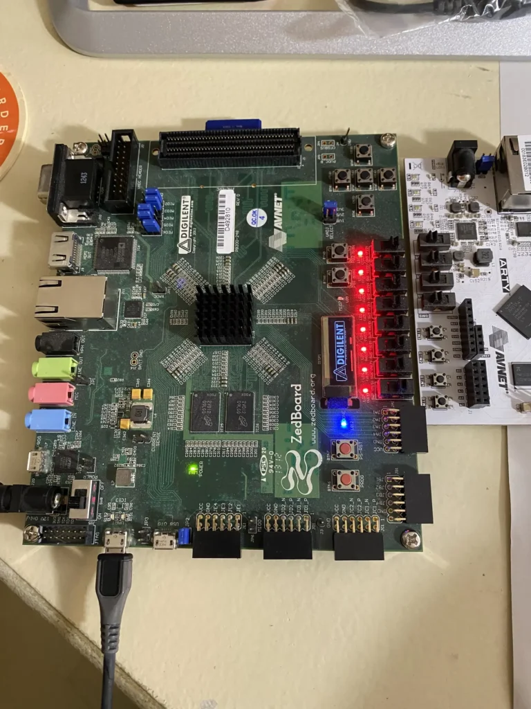 Digilent ZedBoard FPGA development board with red LEDs, buttons, and USB cable connected on a desk.