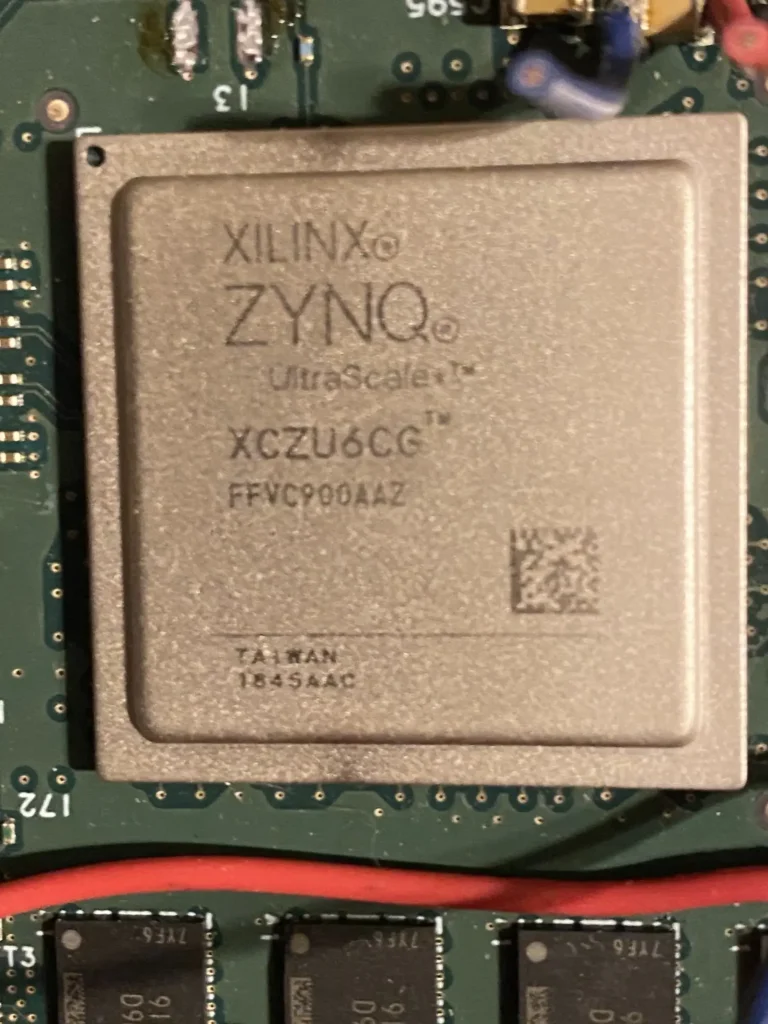 Xilinx Zynq UltraScale+ XCZU6EG FFVC9002 FPGA chip on green PCB with nearby components and red wire.