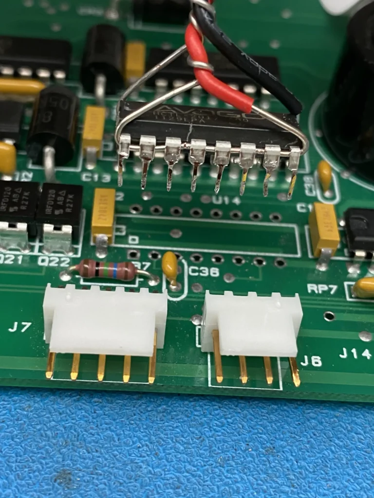 Close-up of green PCB with DIP IC, white pin headers, resistors, and red-black wiring on blue mat.