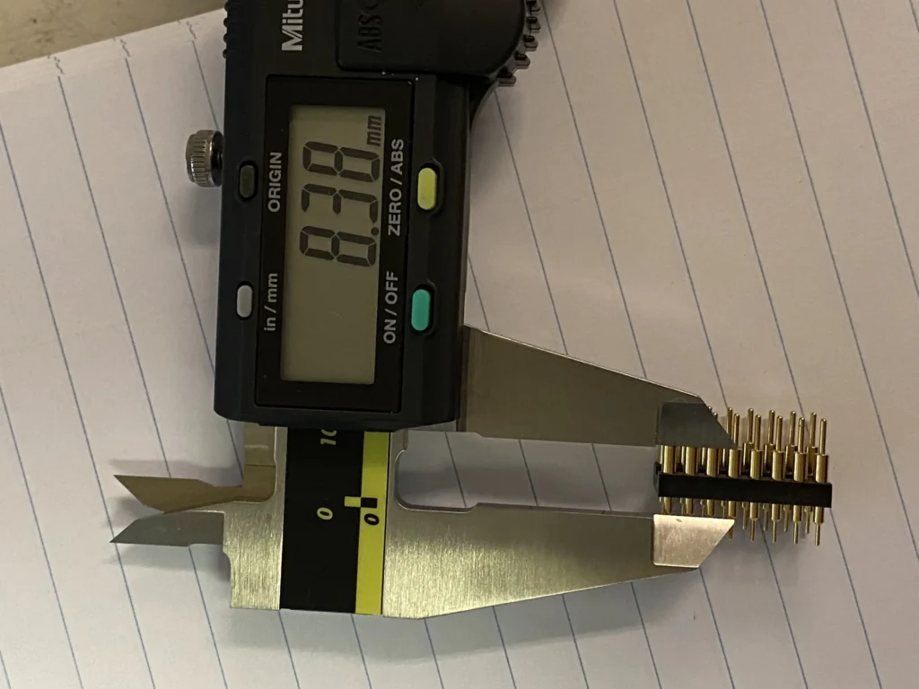Mitutoyo digital caliper measuring gold-plated pin header connector displaying 8.30 mm on lined paper.