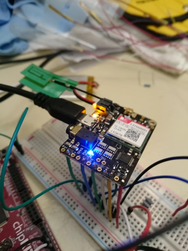 Adafruit FONA GSM module wired to a red Circuit Playground and green breadboard with USB power and antenna.
